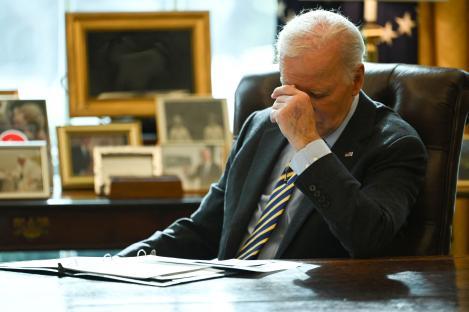 President Biden sits at his desk, appearing concerned.