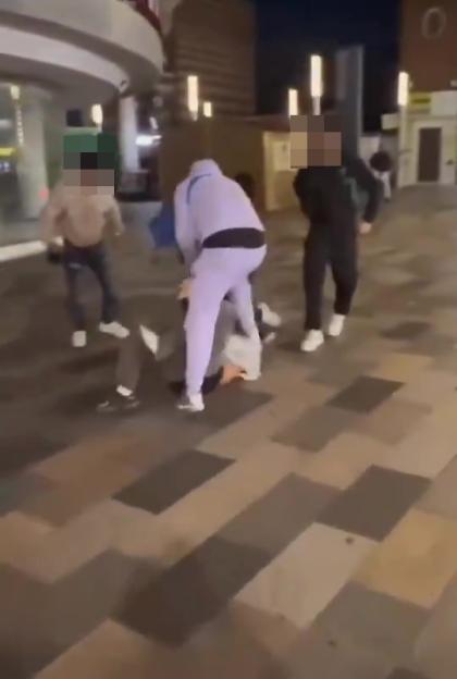 A group of people assaulting an individual lying on the ground on a street.