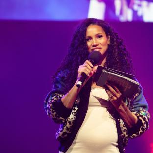 Vick Hope speaking at an event, holding a microphone and a book.