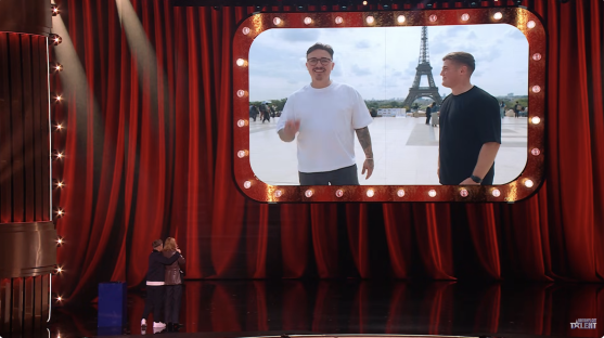Screenshot of two men in Paris shown on a large screen on a stage.