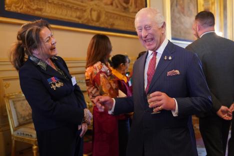 King Charles III laughing and talking to a woman at a reception.