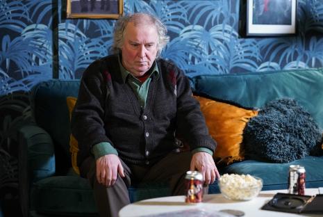 Nigel from EastEnders sitting on a couch.