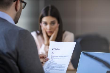 A nervous job applicant sits across from an interviewer who is reviewing her resume.