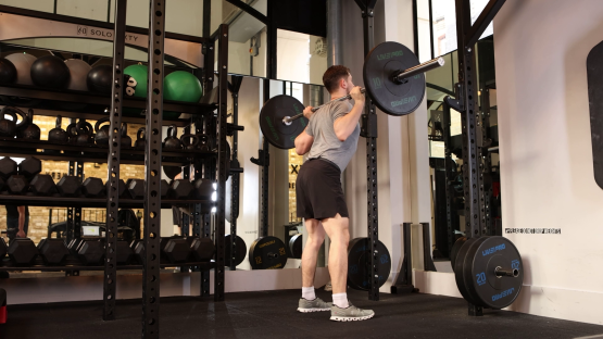 Man performing barbell back squats in a gym.