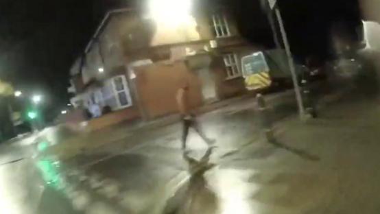 Bodycam footage of a man wielding a knife on a street at night.