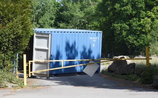 Blue shipping container with its door open, partially blocked by a yellow gate.