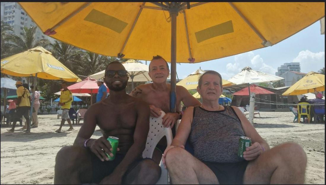 Yostin Andres Mosquera, Albert Alfonso, and Paul Longworth sitting under a yellow beach umbrella.