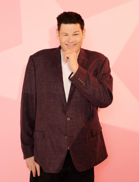 Mark Labbett from Celebs Go Dating, smiling and touching his chin.