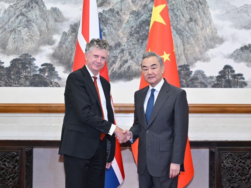 Wang Yi and Jonathan Powell shaking hands in front of Chinese and British flags.