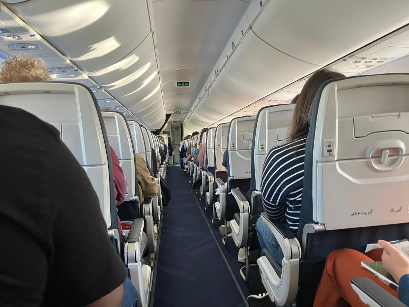 Airplane aisle with rows of mostly empty seats, viewed from the perspective of a seated passenger.