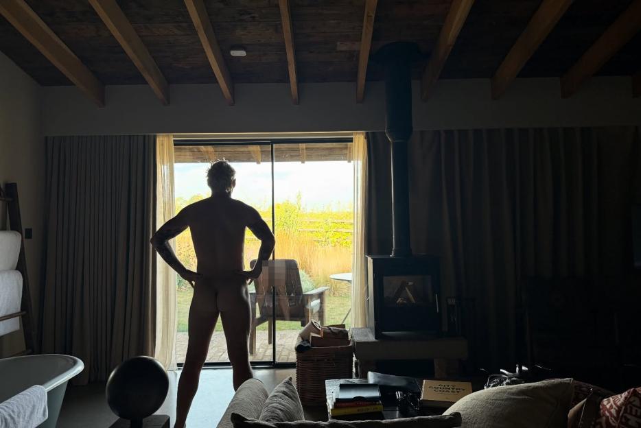 Photo of a nude man standing in front of a window.