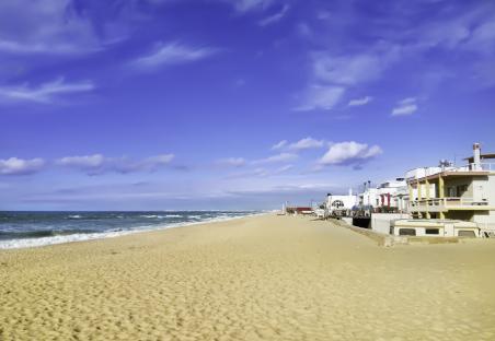 Sandy beach in Faro, Portugal, with ocean waves and buildings in the background.