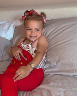 Toddler girl sitting on a bed holding a red bag.