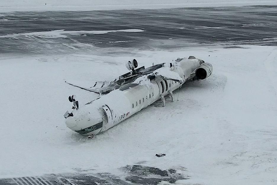 Drone view of the wreckage of a Delta Air Lines CRJ-900 aircraft crashed on a snowy runway.
