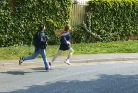 Two teenagers running down a street.