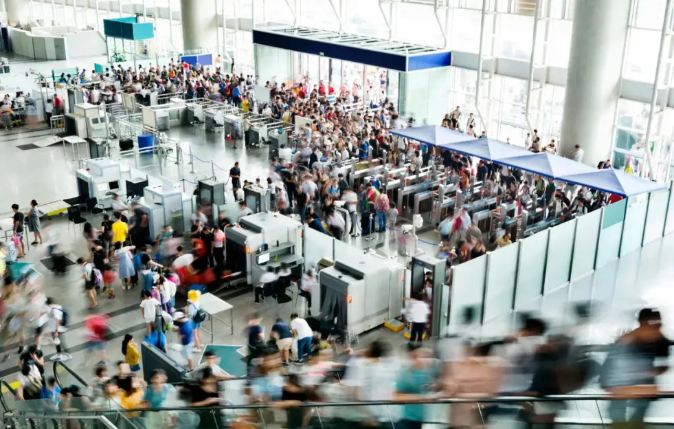 A crowded railroad station lobby with people moving through security checkpoints.