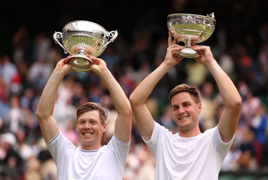 Two tennis players holding up trophies.