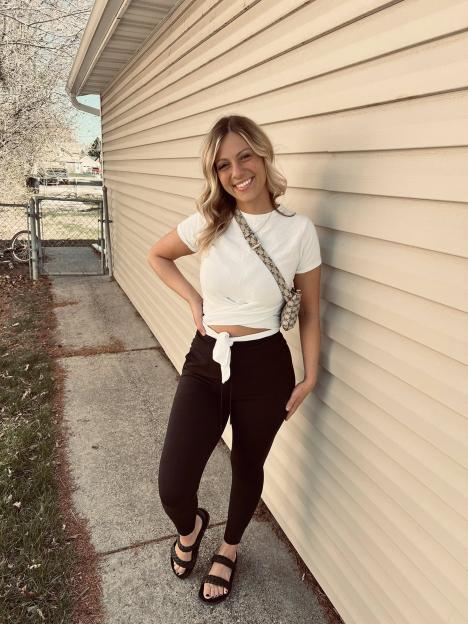 Raylee Reinhart posing outdoors, leaning against a house with light-colored siding.