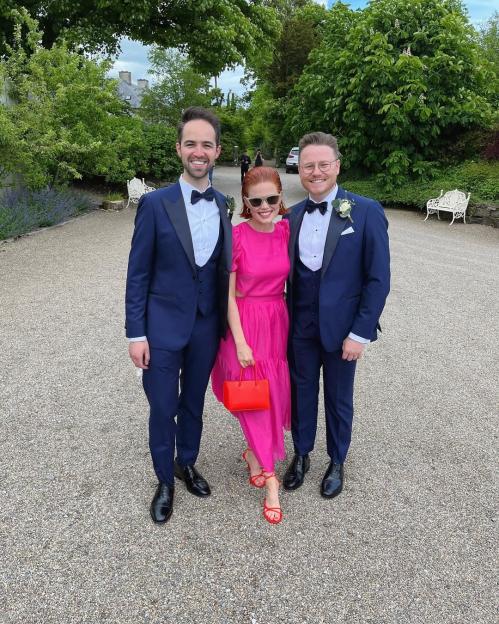 A woman in a pink dress with two men in suits.