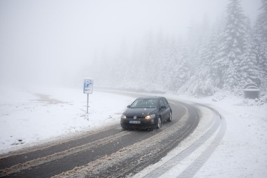 A black car drives on a snow-covered road on a mountain.