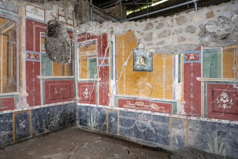 Pompeii wall painting showing a partially destroyed room with colorful frescoes.