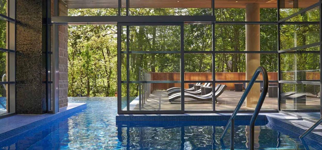 Indoor spa pool at Centre Parcs Woburn with a view of an outdoor lounge area and lush trees.