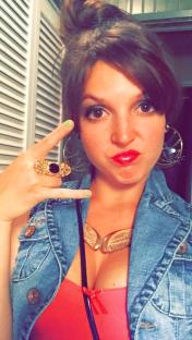 Woman making peace sign, wearing denim vest and gold jewelry.