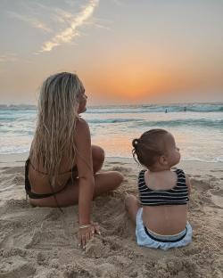 Woman and toddler sitting on beach at sunset.