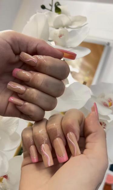Close-up of two hands with long, nude-colored nails decorated with pink tips and white, wavy designs.