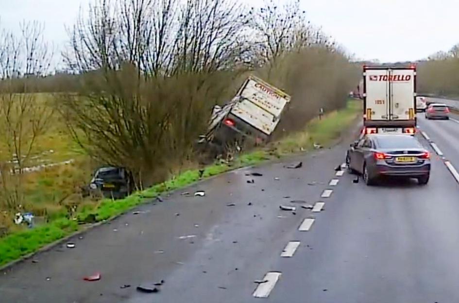 Dashcam footage of a box van crashed into a layby, with debris on the road and another car parked in the distance.