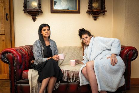 A solicitor and a mother of three sit on a couch; the mother is in a bathrobe.