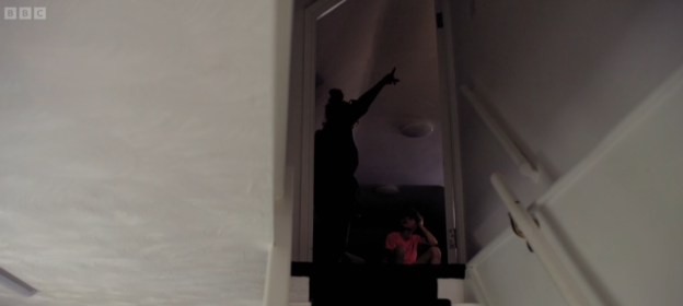 Silhouette of a person pointing up the stairs at another person sitting on the stairs.