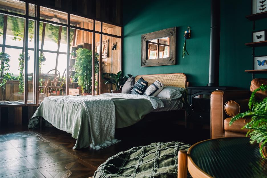 Loft bedroom interior with a green wall, rattan furniture, plants, and a large window.
