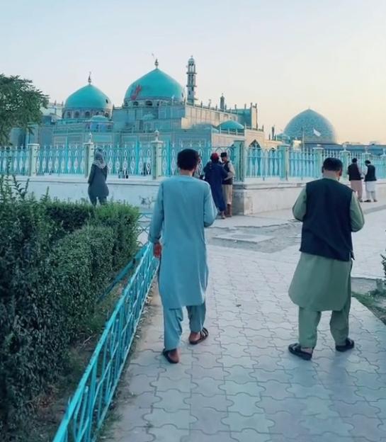 People walking on a path with the Hazrat-e-Ali shrine or the blue mosque in Mazar-i-Sharif in the background.