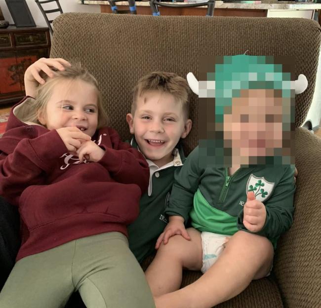 Photo of three young children sitting on a couch; one child's face is blurred.