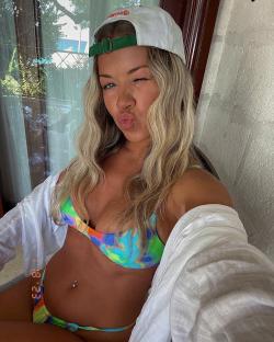 Woman in bikini and baseball cap blowing a kiss.