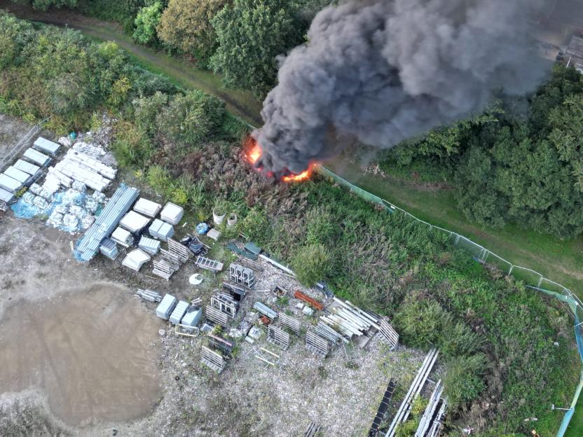 Aerial view of a fire with black smoke rising from overgrown vegetation next to a construction site.