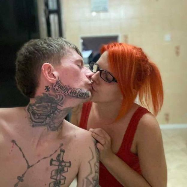 Couple kissing; man has face and neck tattoos.