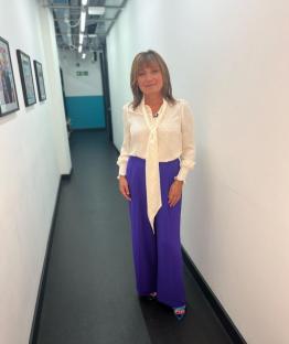 Lorraine Kelly in purple trousers and a white blouse.