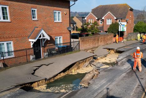 Large sinkhole in a road, cordoned off by police.