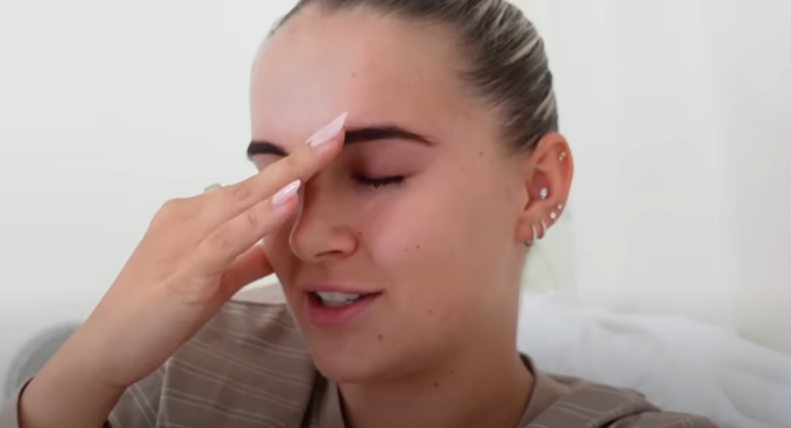 A young woman touching her forehead with her eyes closed.