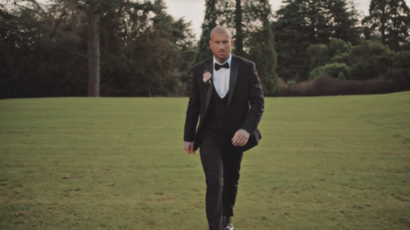 A groom walking on a grassy field, looking forward.