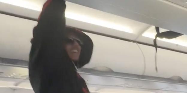 Person stowing luggage in airplane overhead bin.