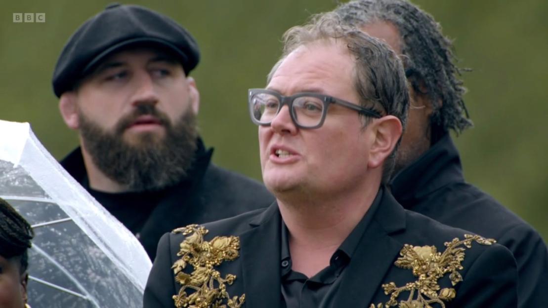 Alan Carr speaking in a black jacket with gold embroidery.