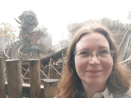 Woman in glasses in front of a wooden rollercoaster.