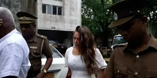 A young woman in a white dress escorted by police officers.
