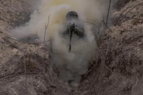 Azov Brigade soldier in a trench during military training amidst smoke.