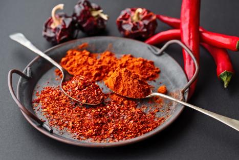 Spanish paprika and pepper powder in spoons and on a tray, with fresh chili peppers.