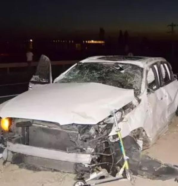 A wrecked car on the side of a road at night.