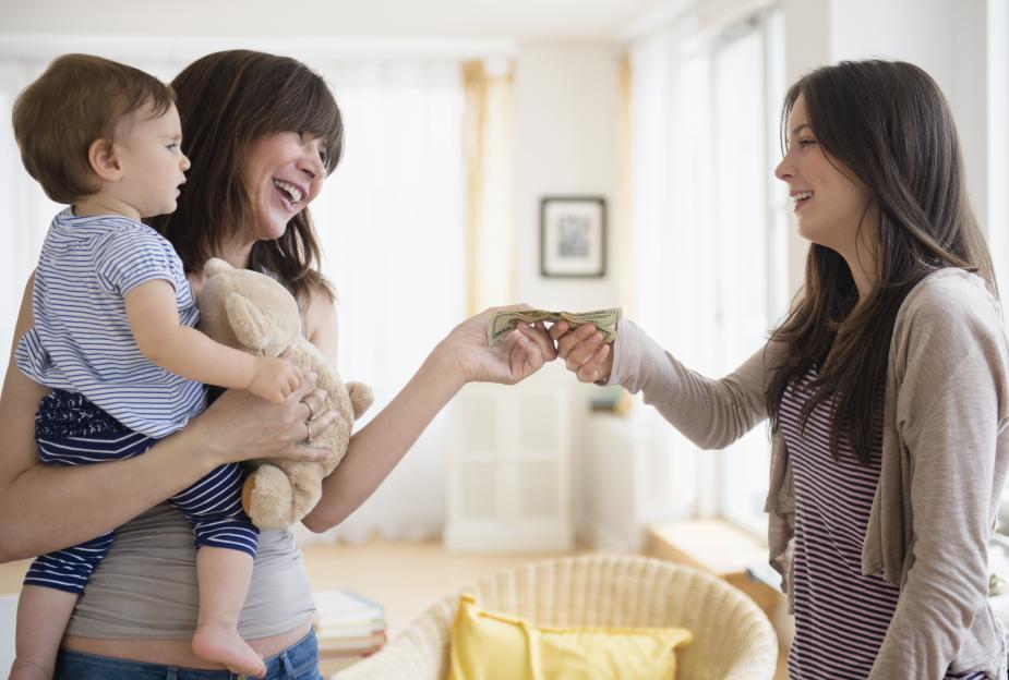 A woman handing money to another woman while holding a baby.